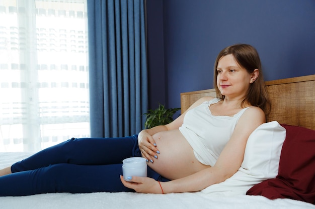 Беременная женщина в постели со специальным кремом для живота для защиты кожи