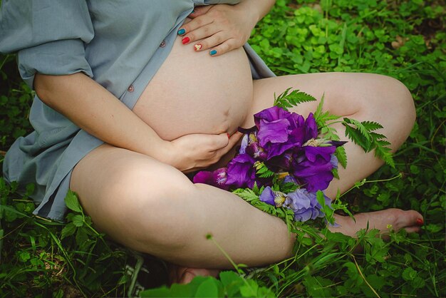 Pregnant Woman Belly Pregnancy Concept Over green nature blurred Background Pregnant tummy close up Expectant female touching tummy outdoor in spring park holding bunch of dandelions Sun light