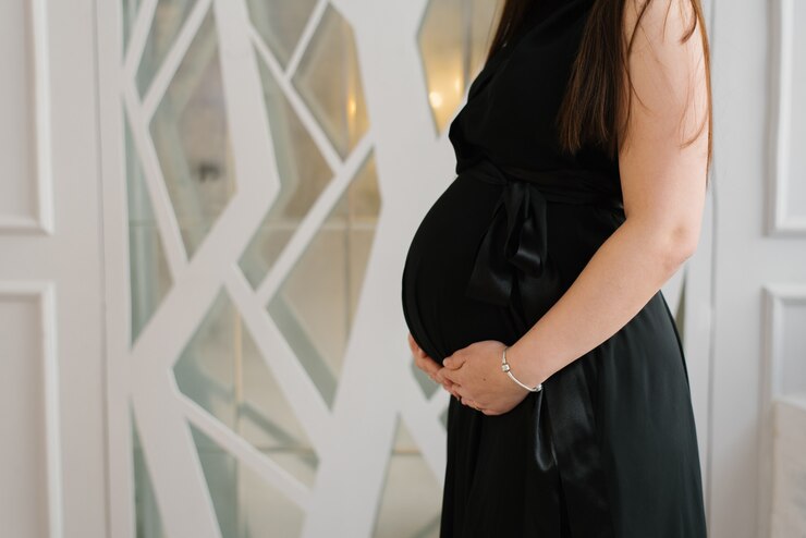 Photo 黒のドレスを着た妊婦は、彼女の手をおなかの上に保持します。コピースペース