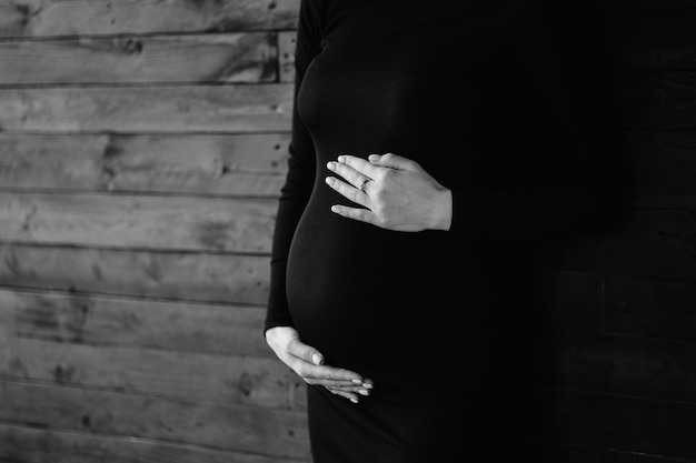 a pregnant woman in black is standing in front of a wooden wall