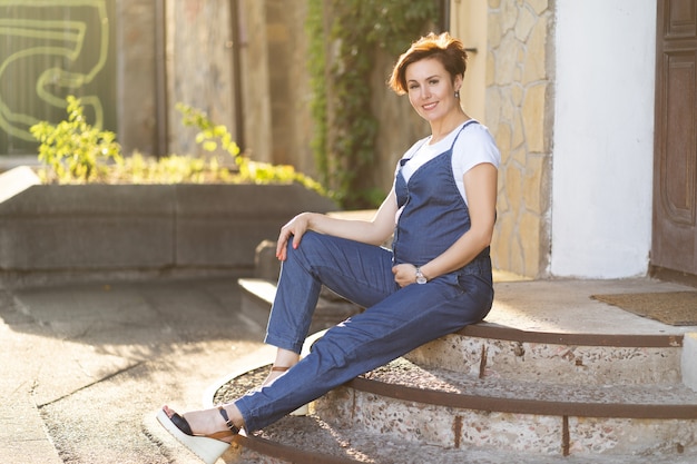 Foto donna incinta in tuta blu che si siede sui gradini all'aperto