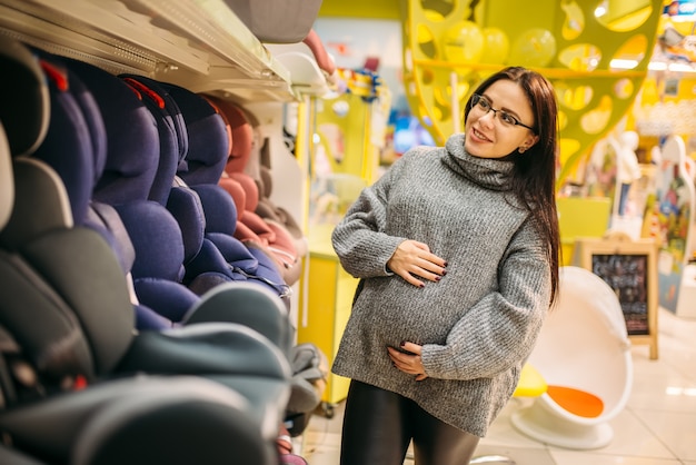 Pregnant woman choosing child car seat in store