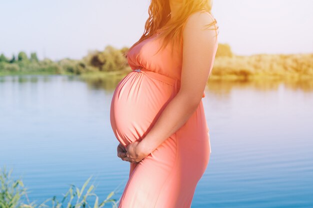 Pregnant woman close up tummy on beach in pink dress