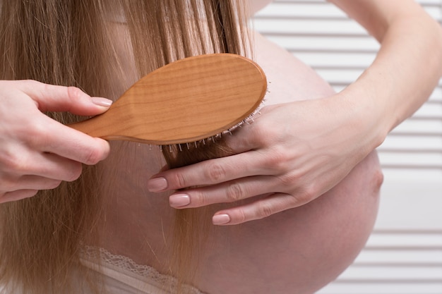 Foto donna incinta che pettina i suoi capelli lunghi. avvicinamento. concetto di salute