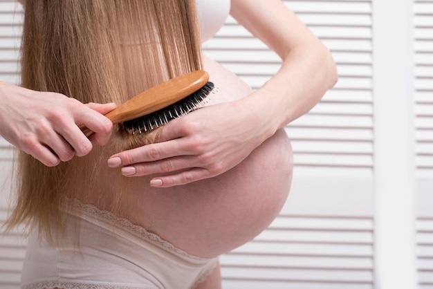 Pregnant woman combing her long hair. Close-up. Health 