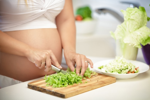 Pregnant woman cuts lettuce on wooden Board