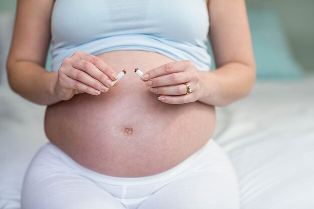 Pregnant woman cutting a cigarette in two in her bedroom