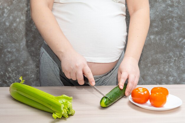 Donna incinta che taglia cetriolo per insalata verde fresca, femmina prepara una gustosa cena biologica a casa