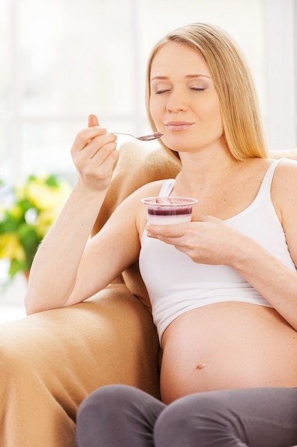 Foto sogno ad occhi aperti della donna incinta. donna incinta felice che si siede sulla sedia e che mangia yogurt