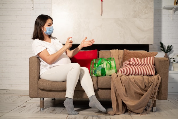 A pregnant woman disinfects her hands and puts on a protective face mask