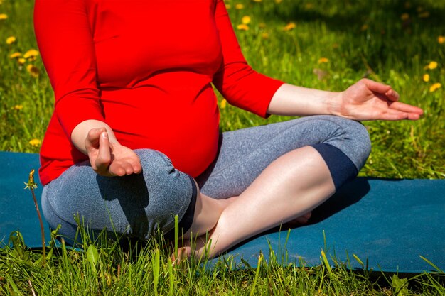 Pregnant woman doing asana sukhasana outdoors