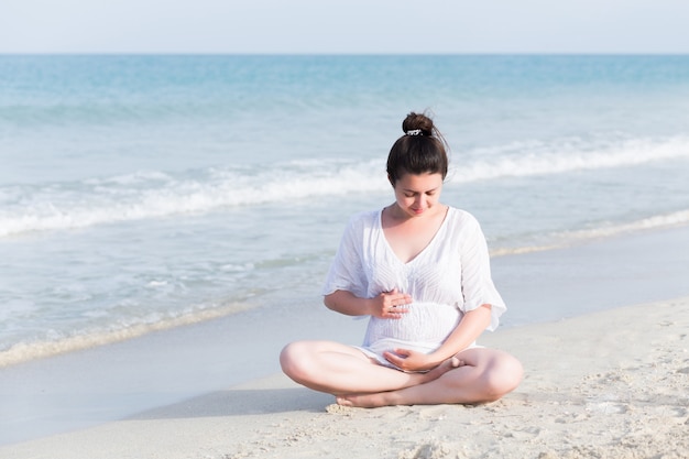 Pregnant woman doing yoga exercises on the beach