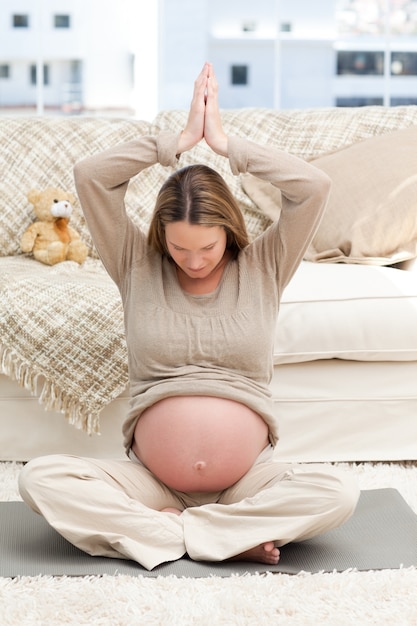 Беременная женщина делает йогу на полу своей гостиной