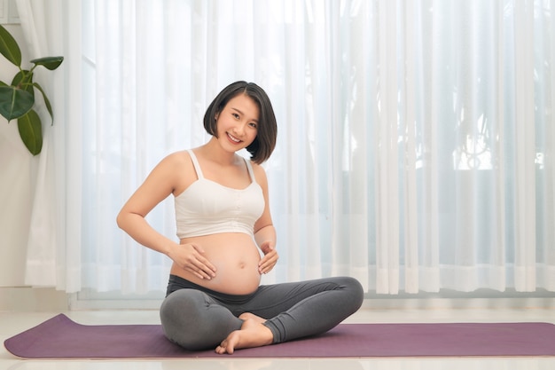 妊娠中の女性がリビングルームでヨガをやって