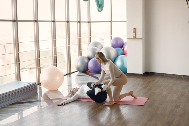 Pregnant woman doing yoga with personal trainer Yoga trainer assisting pregnant woman while doing exercises Blonde pregnant woman wearing white clothes