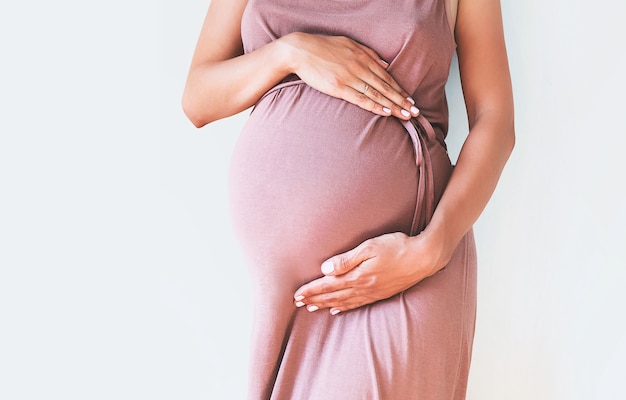 Pregnant woman in dress holds hands on belly on a white background Pregnancy maternity