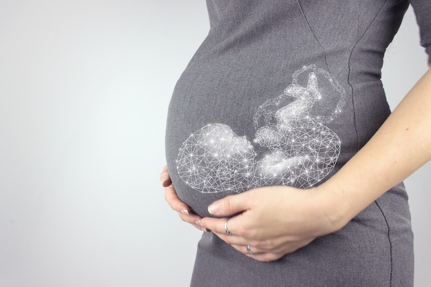 La donna incinta in vestito tiene le mani sulla pancia con il feto dell'ologramma