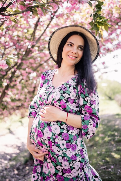 Pregnant woman in a dress with black hair near cherry blossoms in spring