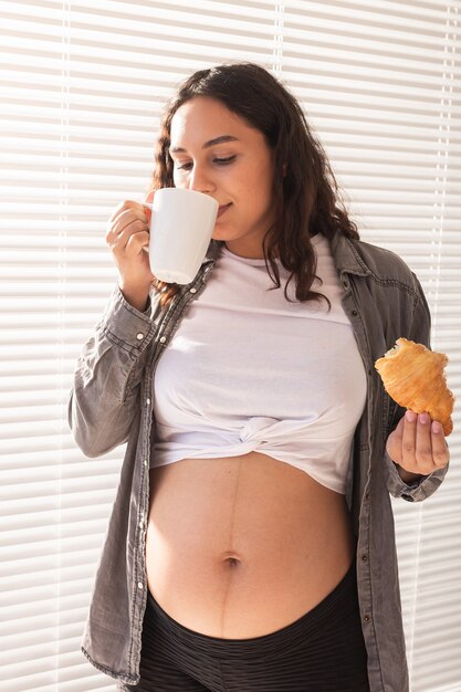 Pregnant woman drinking tea and eating croissant during lunch