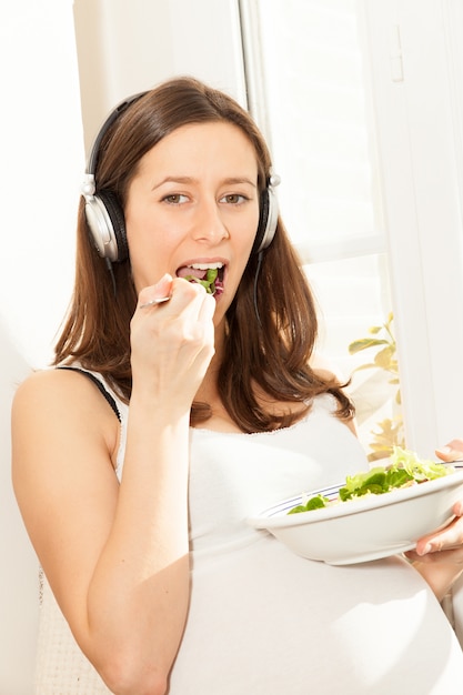 Pregnant woman eat salad and listening to music