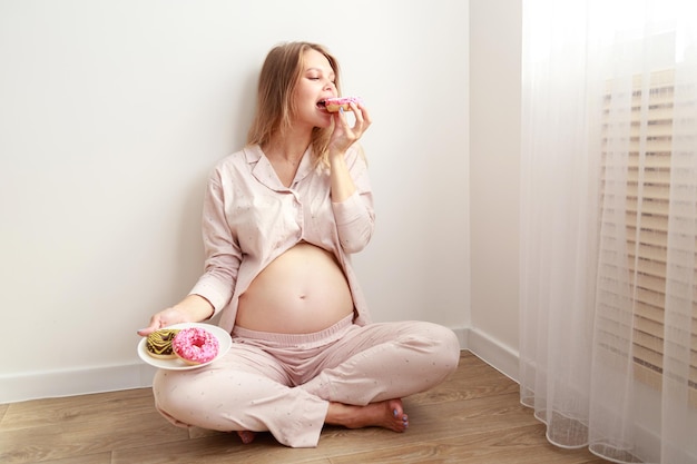 Foto donna incinta che mangia la ciambella sul pavimento a casa