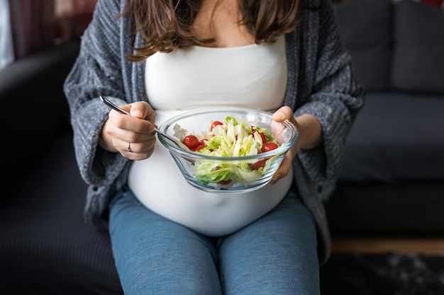 소파에 앉아 신선한 야채 샐러드를 먹는 임산부 건강한 임신 개념