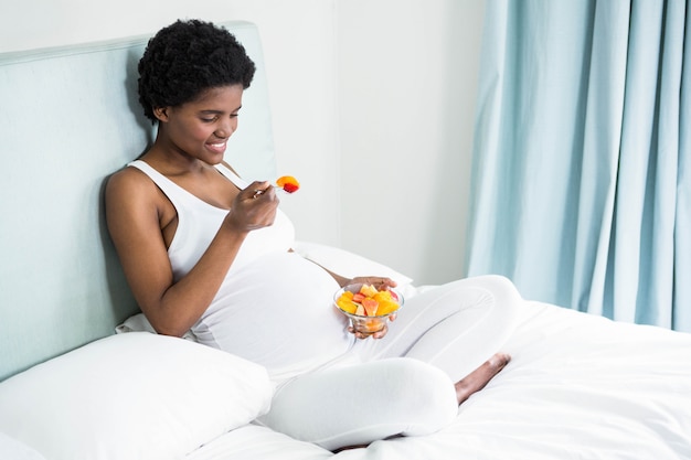 Pregnant woman eating fruit salad lying on her bed