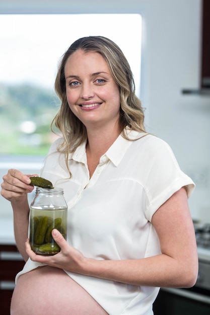 Pregnant woman eating gherkins in the kitchen