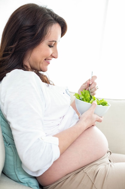 Pregnant woman eating salad on couch