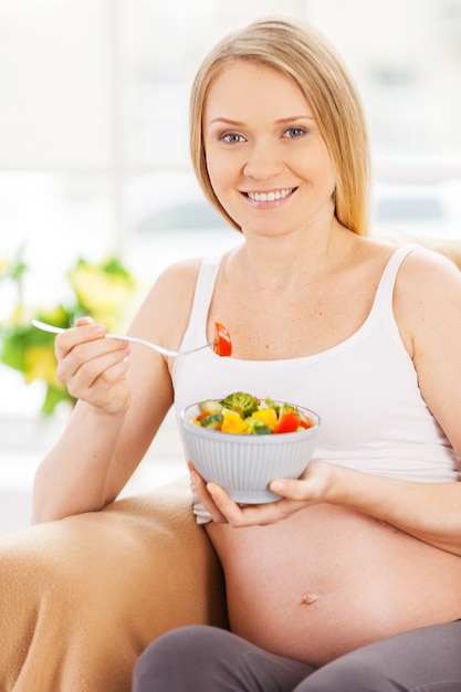 Pregnant woman eating salad. Happy pregnant woman sitting on the chair and eating salad