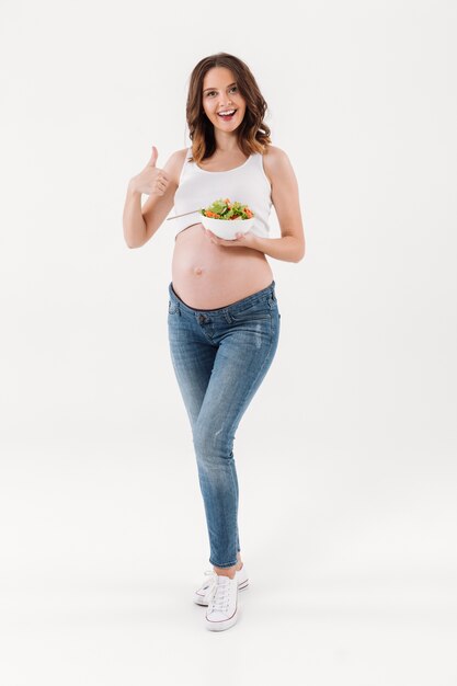 Беременная женщина ест витамин салат показывает палец вверх.