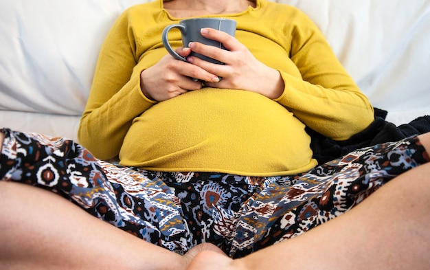 Pregnant woman enjoy cup of tea while sitting on sofa after yoga practice at home Relaxing break for desperate pregnant woman