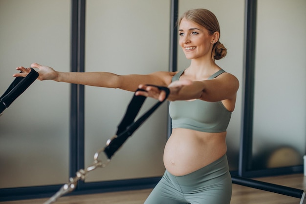 Donna incinta che si esercita con l'aiuto del riformatore durante la lezione di pilates