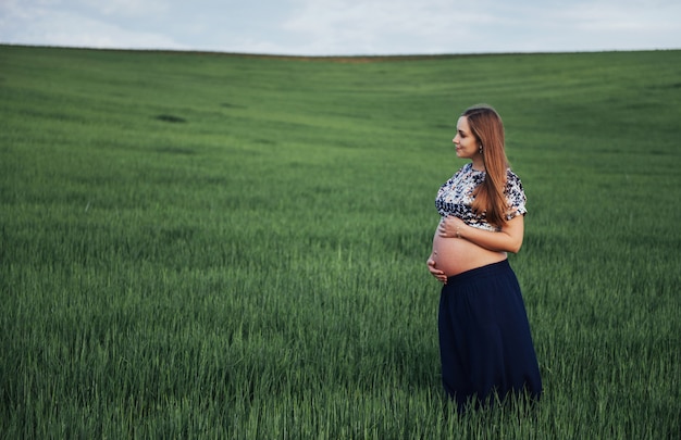 Беременная женщина в поле зеленой пшеницы