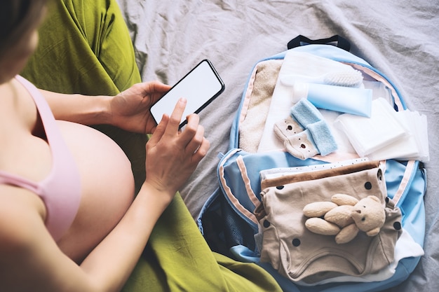 pregnant woman getting ready for labor packing stuff for hospital making notes in smartphone