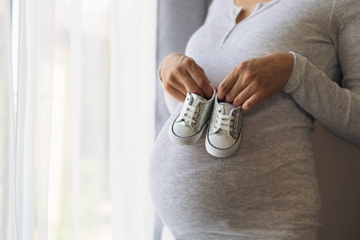 Photo pregnant woman in gray jacket holds baby shoes in hands on pregnant belly, waiting baby concept, baby shopping, new life