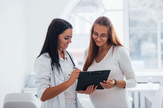 Pregnant woman have visit with obstetrician indoors. Signing documents.