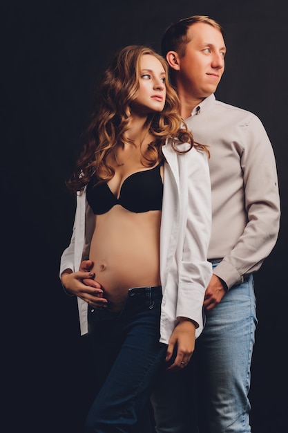 Pregnant woman her husband holding her tummy.Beautiful belly of young attractive pregnant woman over black background.