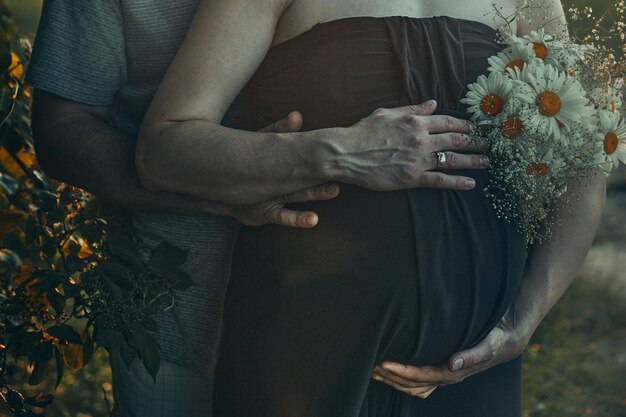 Pregnant woman and her husband hugging her tummy standing outdoors surrounded by nature