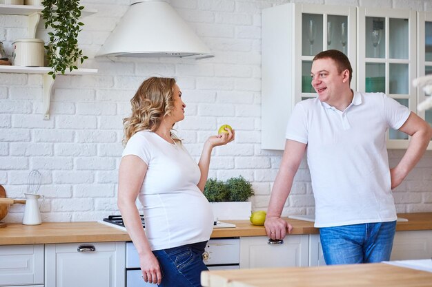 Pregnant woman and her husband in the kitchen at home with fruit.