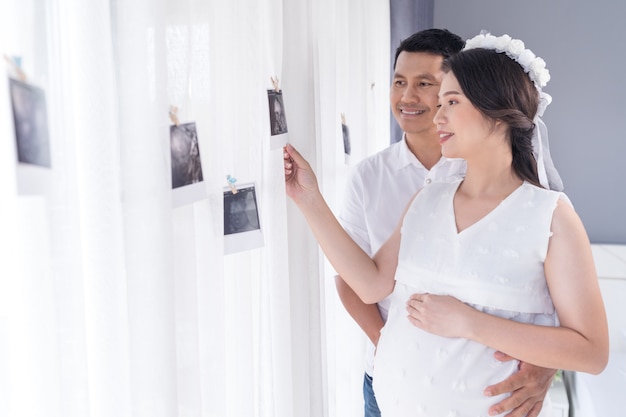 Беременная женщина и ее муж смотрят фото УЗИ на окне