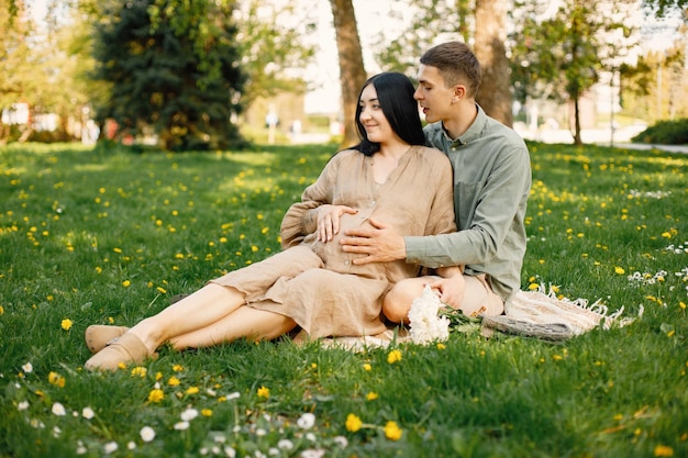 Pregnant woman and her husband sitting in a park on a grass and hugging