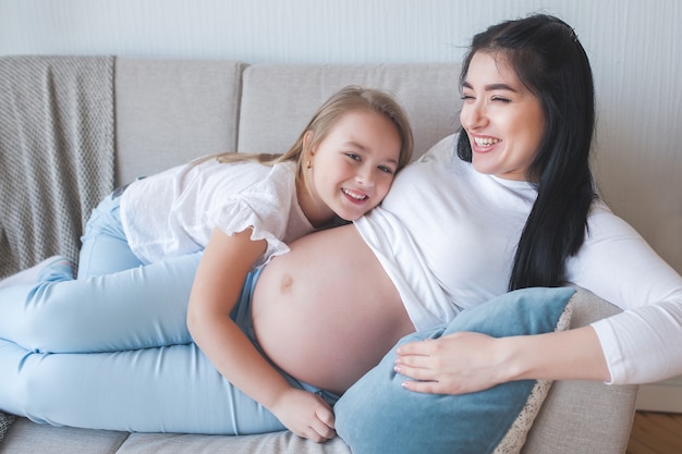 Pregnant woman and her little daughter having fun indoors. Maternity. Young mother waiting for a baby birth with little cute daughter. Family together.