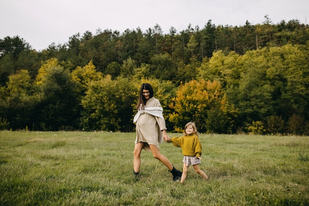 Pregnant woman and her toddler daughter outdoors walking in a field with green grass