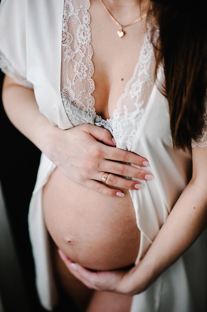임신한 여자는 손을 잡고 배를 동그랗게 껴안고 옆으로 서 있는 둥근 배를 껴안고 출산 개념을 닫습니다. 9개월 베이비 샤워