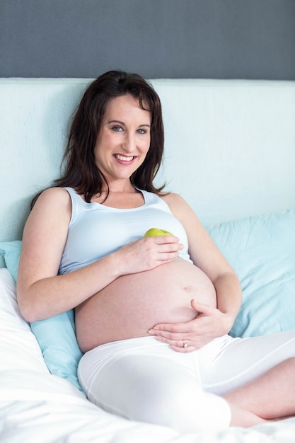 Pregnant woman holding an apple on her belly at home 