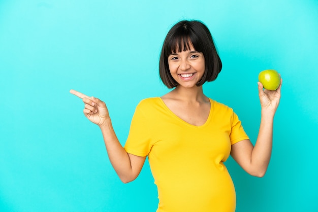 横に指を指している青い背景で隔離のリンゴを保持している妊婦