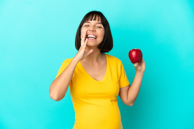 Pregnant woman holding an apple isolated on blue background shouting with mouth wide open