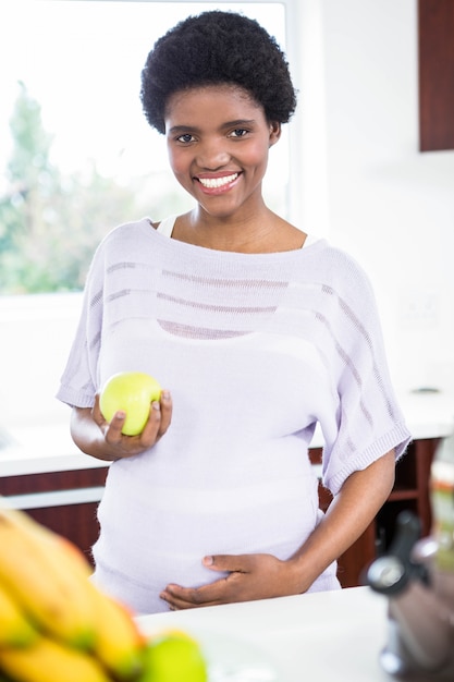 Pregnant woman holding apple in kitchen