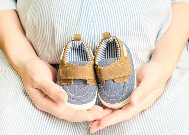 手に赤ちゃんの靴を持っている妊婦マタニティ出生前ケアと女性の妊娠の概念